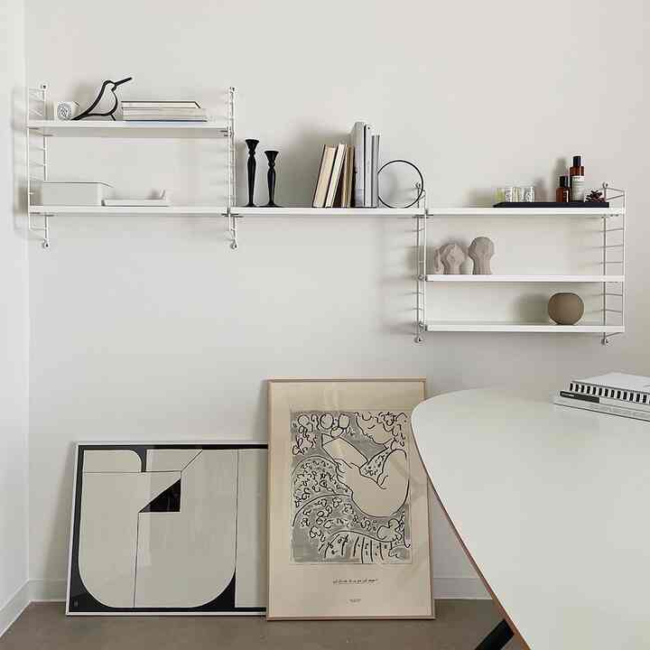 モノトーンの北欧風リビングルーム、白い壁と棚に本やオブジェ、ポスターがセンス良く配置されたミニマルなインテリア