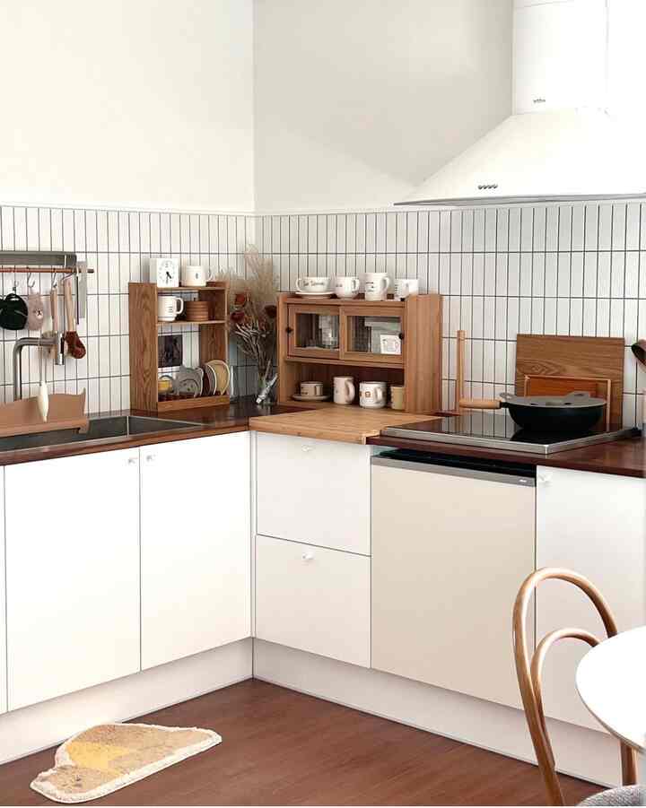 A natural kitchen space featuring white tiled walls and wood tone countertops and shelves with a simple aesthetic