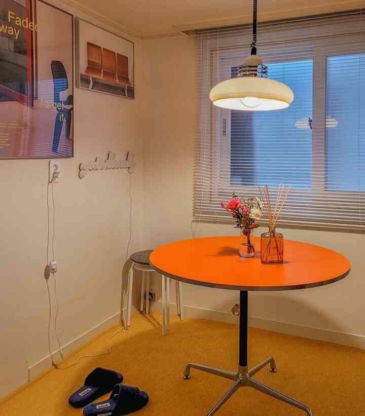 Small cozy kitchen featuring yellow rug, orange round dining table, and white blinds on the window