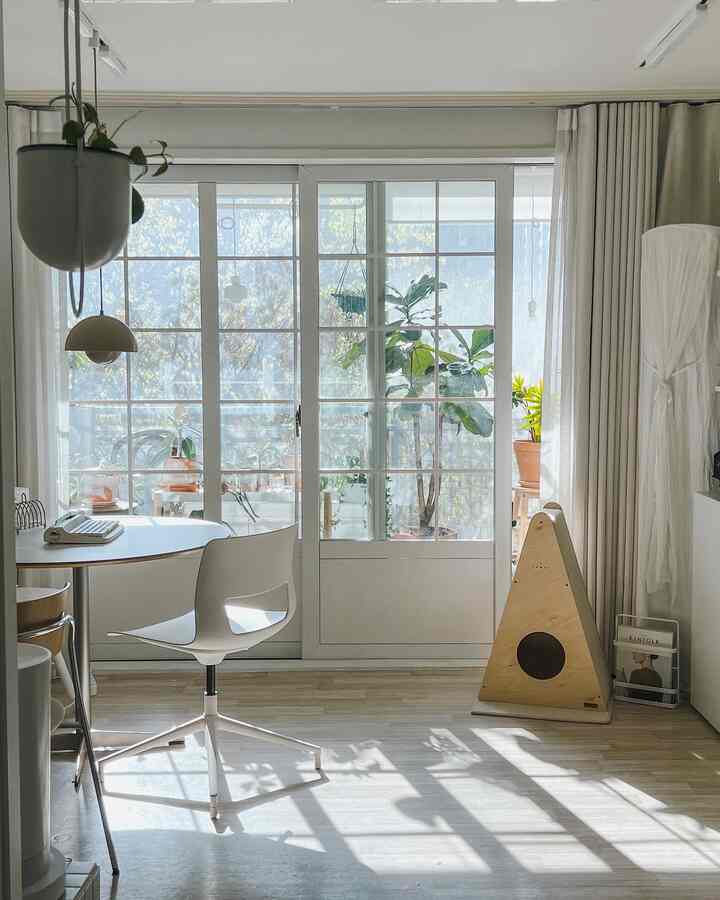 Bright and airy living room and home office in white and natural tones featuring round table, dining chair, and cat scratching post