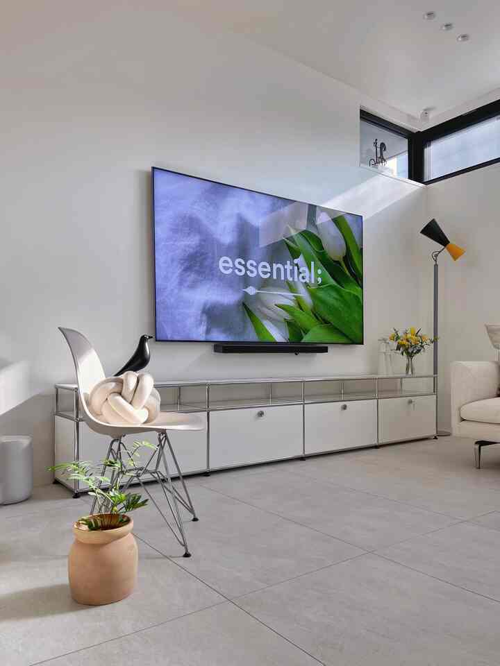 Bright modern living room in white and ivory tones, featuring an Eames plastic chair, large TV, and a floor lamp