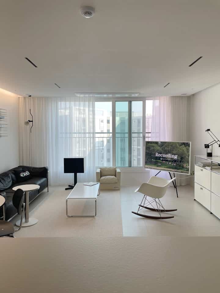 Bright white-tone living room featuring black leather sofa, white armchairs, and coffee table in a modern setting