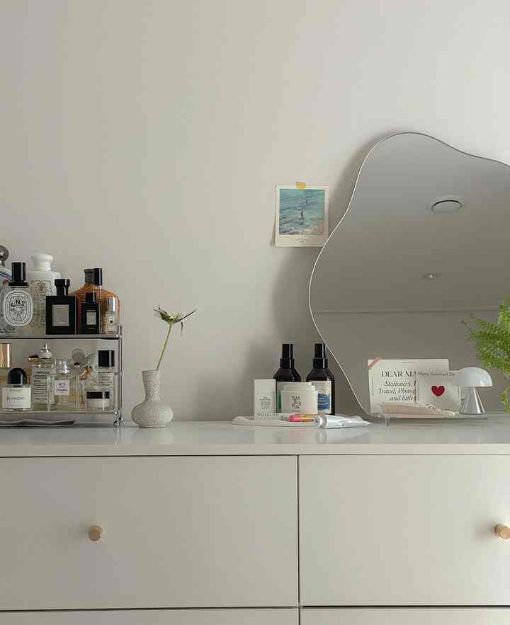 白を基調としたチェストの上に鏡と化粧品が配置されたミニマルなインテリア空間