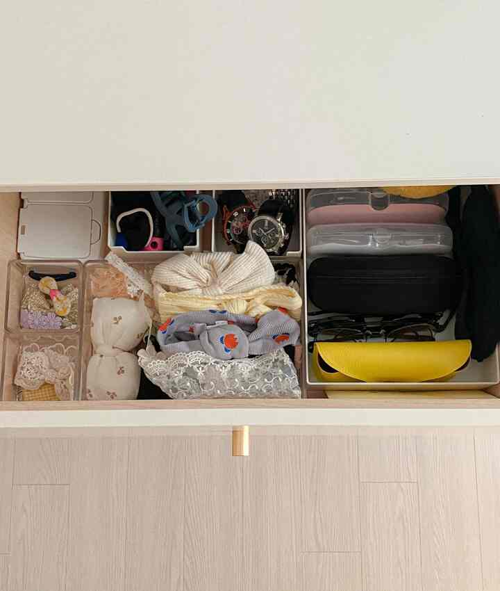 A neatly organized small drawer with white and transparent organizers holding hair accessories, watches, and glasses cases
