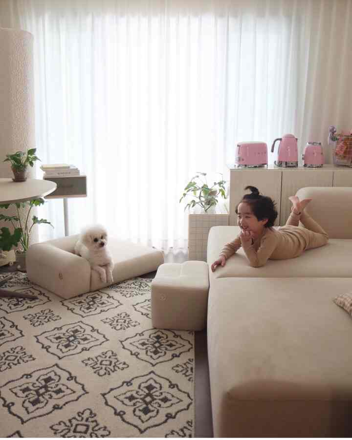 柔らかなベージュとホワイトの色調のリビング、広いソファに子供と犬がくつろぐ雰囲気のあるインテリア