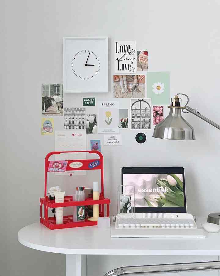 A modern study space in white and red tones featuring a tidy desk setup with a tray and wall decorated with diverse art prints