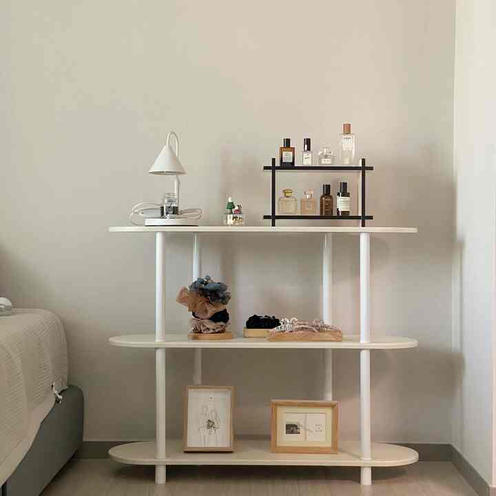 ホワイトとベージュの寝室、シンプルな収納棚と額縁、テーブルランプが配置された清潔感と自然な雰囲気のあるインテリア