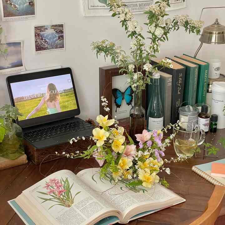 暖かいブラウン調のデスクに花瓶と植物が飾られ、タブレットと本が置かれた北欧風の落ち着いたホームオフィス空間