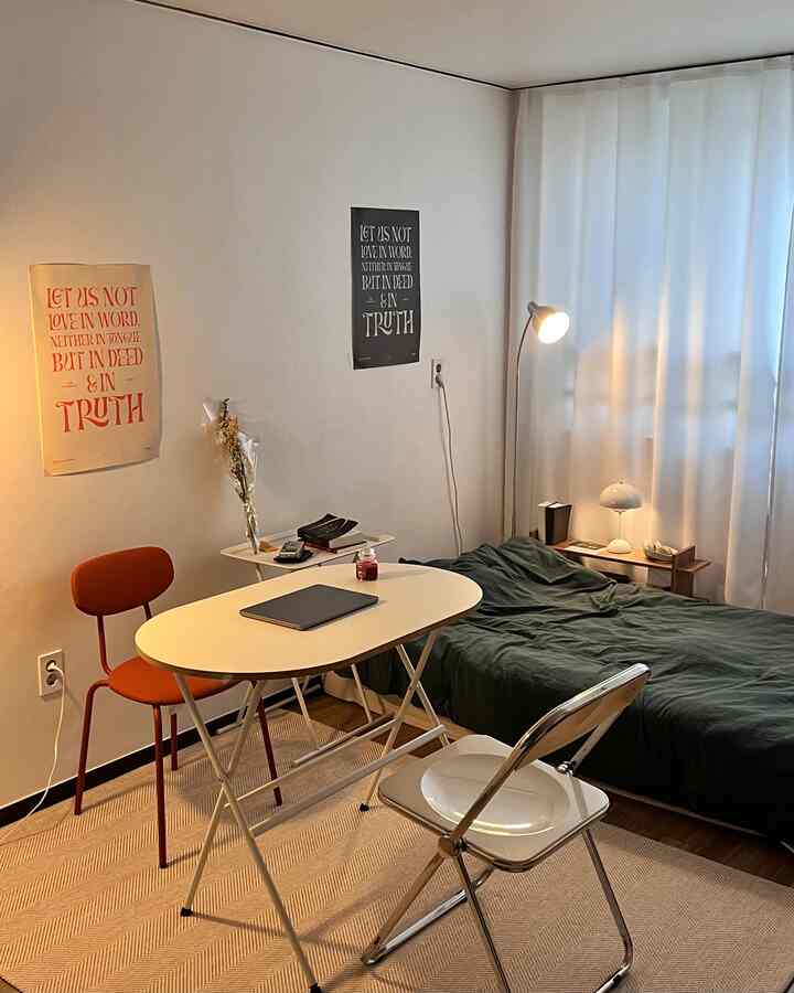 白と茶色のトーンのワンルーム、ミッドセンチュリーモダンスタイルのオレンジの椅子とシンプルなテーブル、ベッドが配置された清潔で居心地の良いインテリア