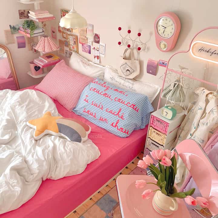Cozy bedroom in pink and white tones featuring a pink bed with cushions and vintage wall clock, creating a lovely atmosphere