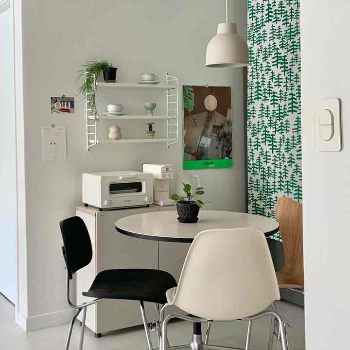 White and green toned kitchen space featuring a round table with mixed chairs in a cozy mid-century modern style