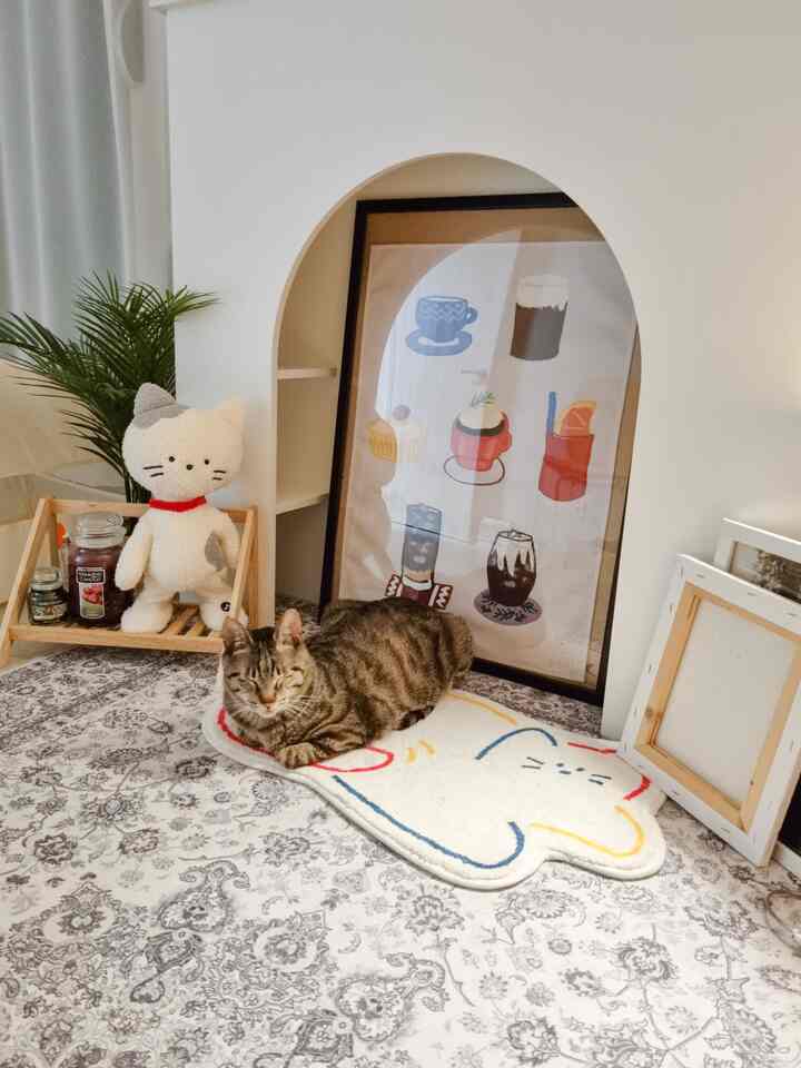 アイボリーとグレーの色調の寝室、猫型ラグとトラ猫、額縁が配置された雰囲気のあるインテリア