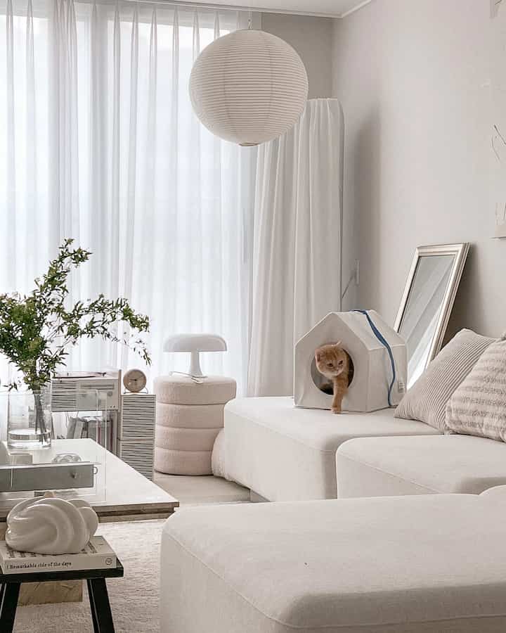 White-toned living room featuring large sofa and a cat hideout, creating a warm and minimal atmosphere