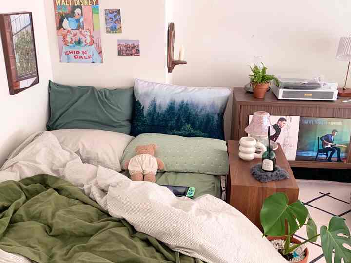 Natural tones with green accents in a studio bedroom featuring a bed, plants, and a turntable creating a cozy atmosphere