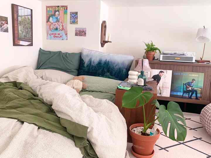 Natural tone bedroom with white walls and green bedding featuring monstera plants and a vintage LP player for cozy atmosphere