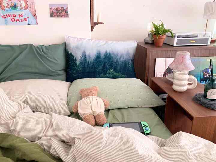 Cozy Nordic bedroom with green bedding and brown wooden furniture, accented by cushions and a record player