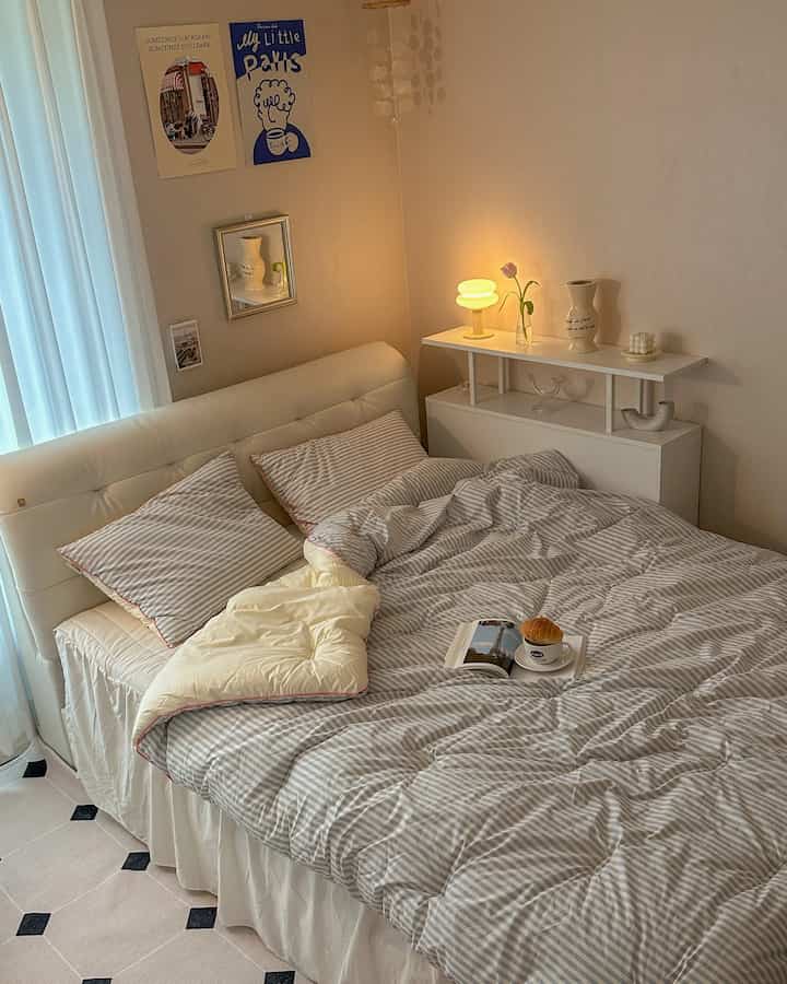 Soft white and sky blue toned bedroom featuring striped bedding and simple French Country style lamp, creating a cozy atmosphere