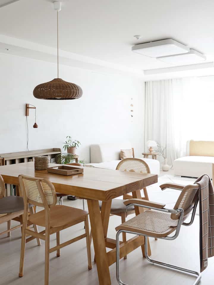 A natural living and dining room with white and wood tones, featuring a wooden dining table and rattan pendant lighting