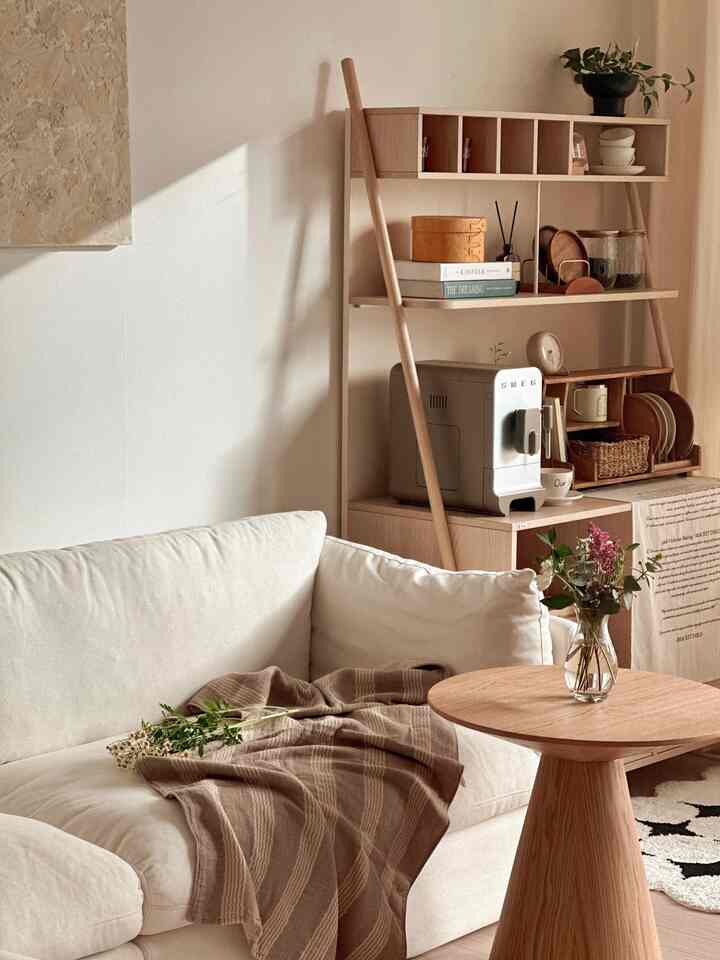Natural wood tones and white living room featuring a cream sofa, round side table, and cafe cabinet creating a cozy home cafe atmosphere