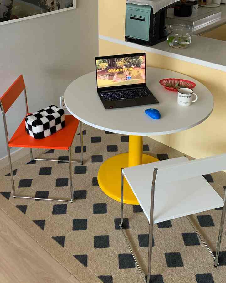 明るいイエローとホワイトのトーンのコンパクトなダイニング、丸テーブルと二脚の椅子、ノートパソコンとワイヤレスマウスが配置されたモダンな空間