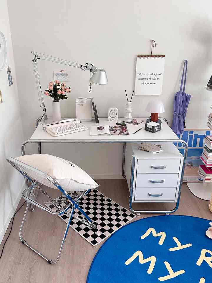 Compact home office space featuring a white desk and transparent chair, set against a white background with a blue round rug