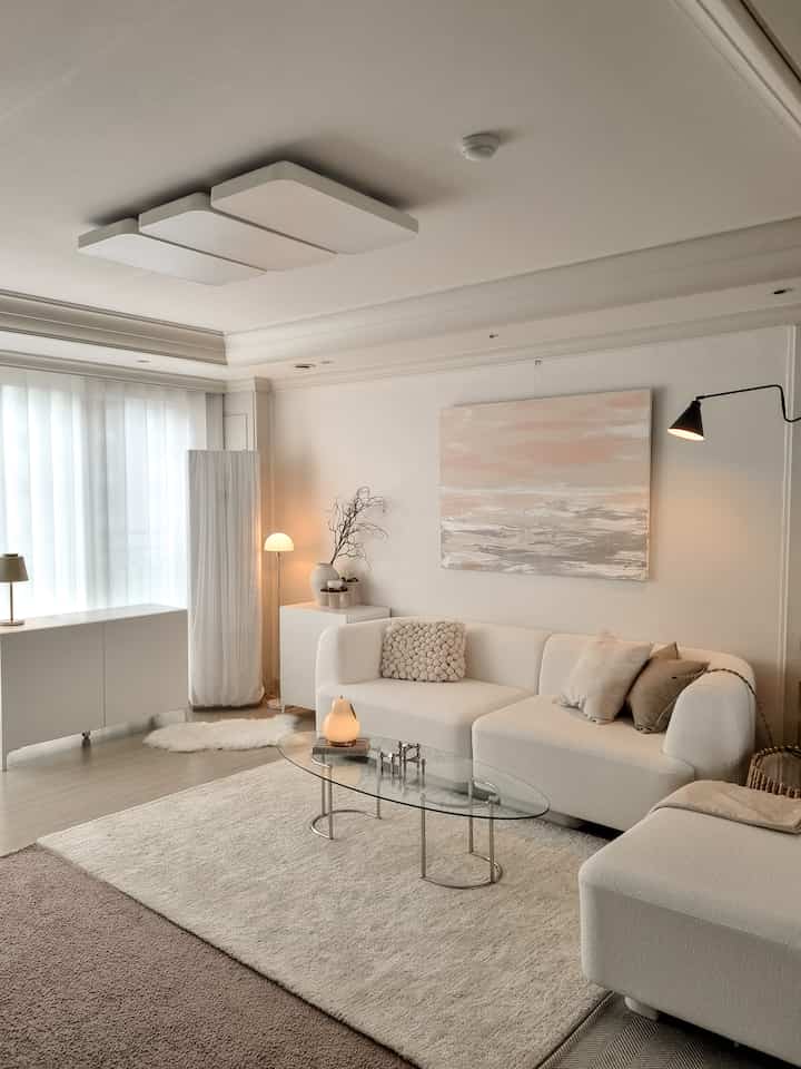 Cozy living room in soft white and beige tones featuring modular sofa and glass coffee table with warm lighting ambiance