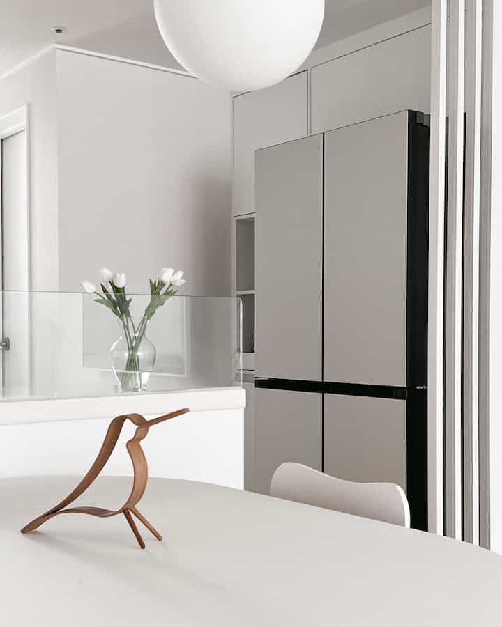 白とグレーのトーンのダイニングルーム、木製オブジェと花瓶が配置されたモダンで清潔感のある空間