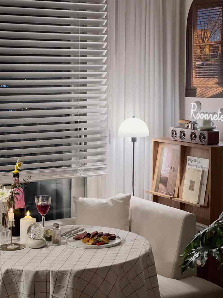 Dining room with white and wood tones featuring a round dining table, cushions, and a floor lamp creating a cozy retro atmosphere