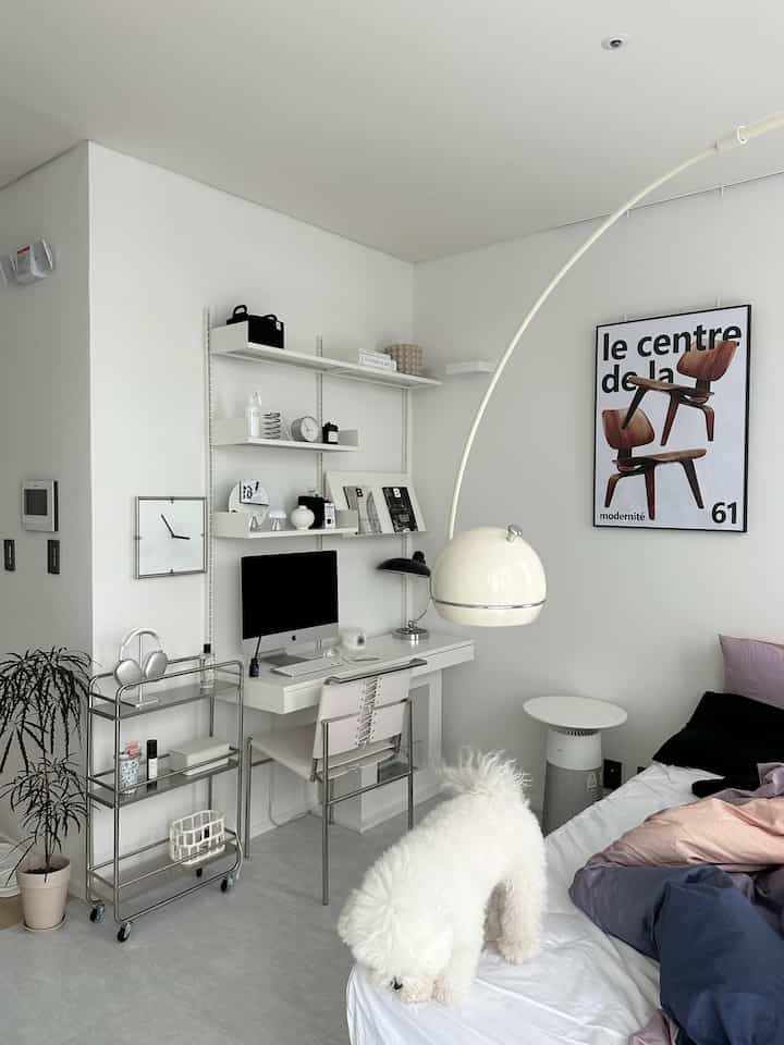 Modern home office space in dominant white tones, featuring shelves, desk, and a dog on the bed, creating a clean and cozy atmosphere