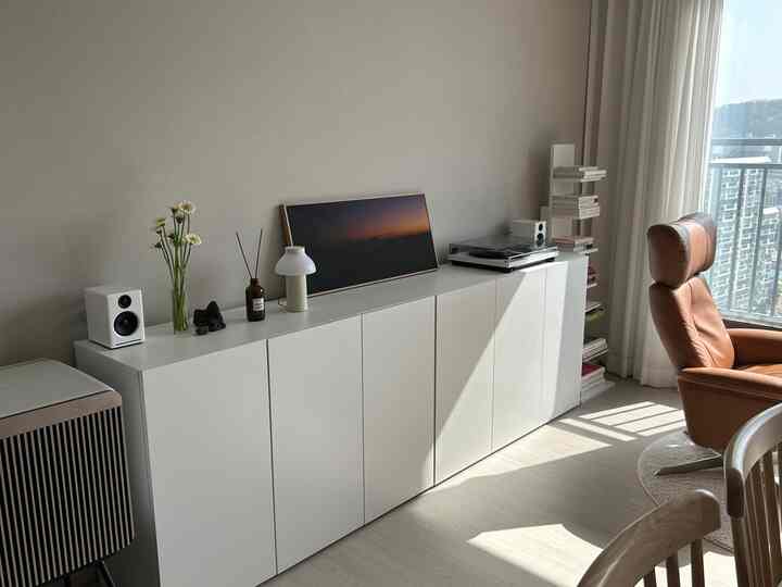 Bright white-toned living room featuring a brown recliner, turntable, and bookshelf, styled in a modern natural aesthetic for a single occupant