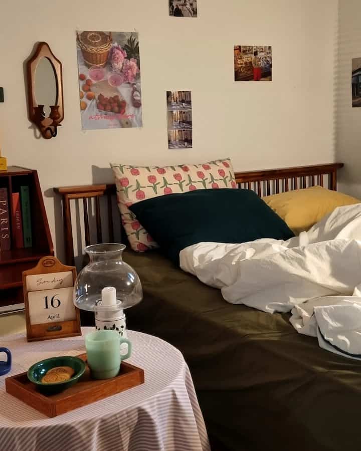 A white and green toned bedroom featuring a wooden bed with floral pillows and a cozy coffee table setup