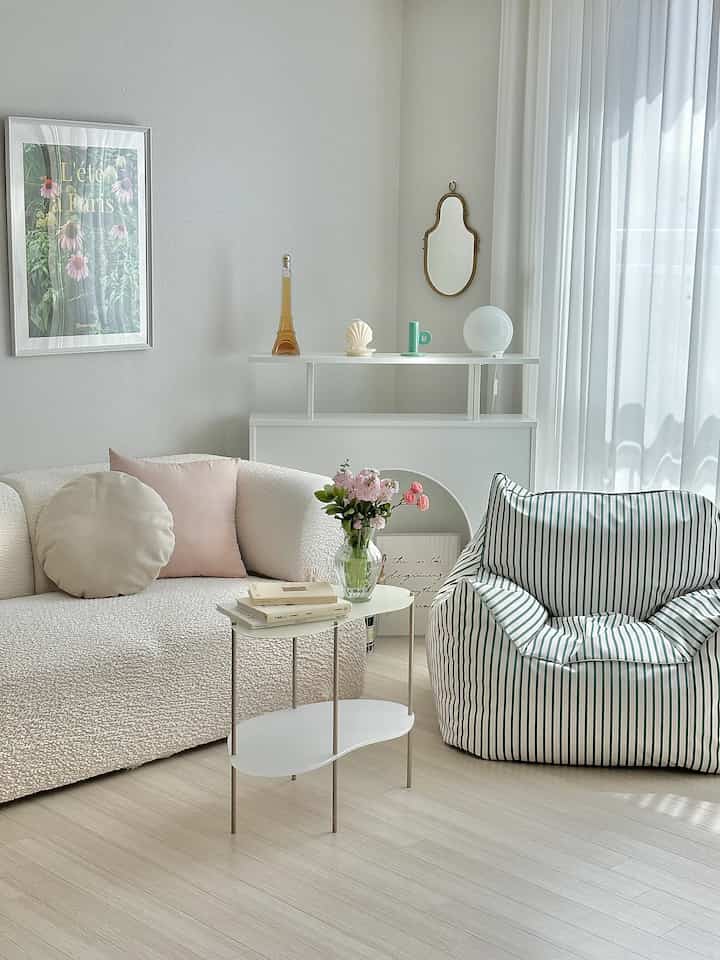 ホワイトとナチュラルカラーのリビング、柔らかな質感のソファとストライプのビーズクッション、ホワイトのサイドテーブルが配置された明るくシンプルな空間