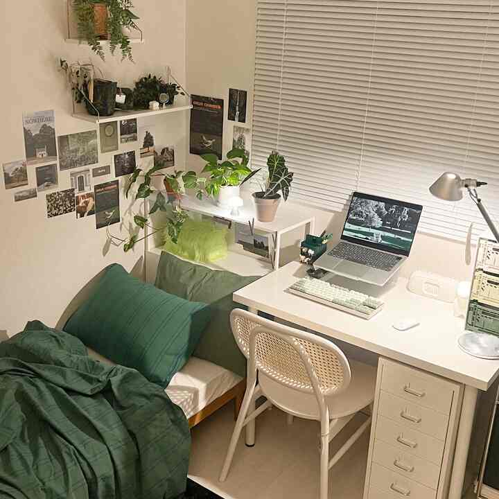 White-toned room with green bedding and plants, featuring a small home office space for a single occupant