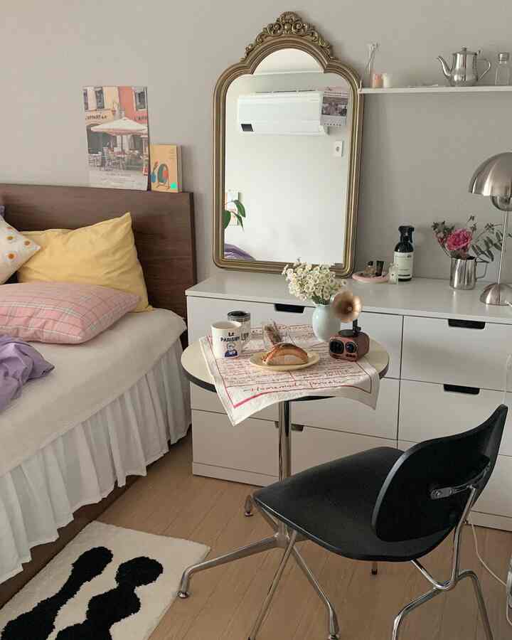 White and brown toned compact bedroom featuring a bed, small coffee table, and decorative gold mirror creating a cozy atmosphere