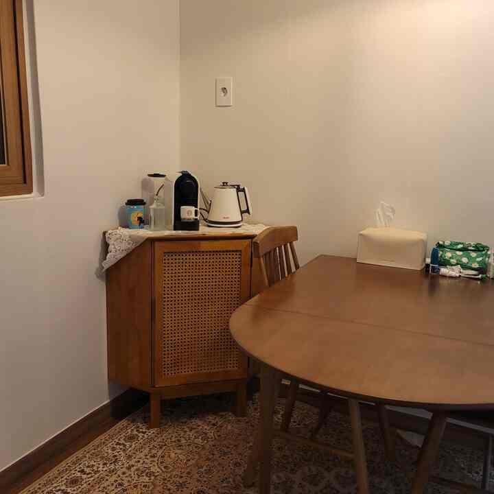 Brown wood-tone dining table with corner rattan wooden storage cabinet against white walls in a compact dining space