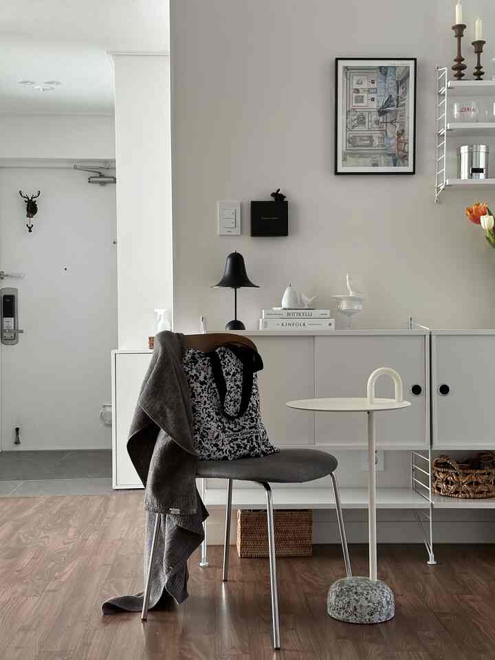 白い壁とブラウンの木目調床が調和したシンプルでモダンな玄関とリビング空間、グレーの椅子と白いサイドテーブルが配置されている