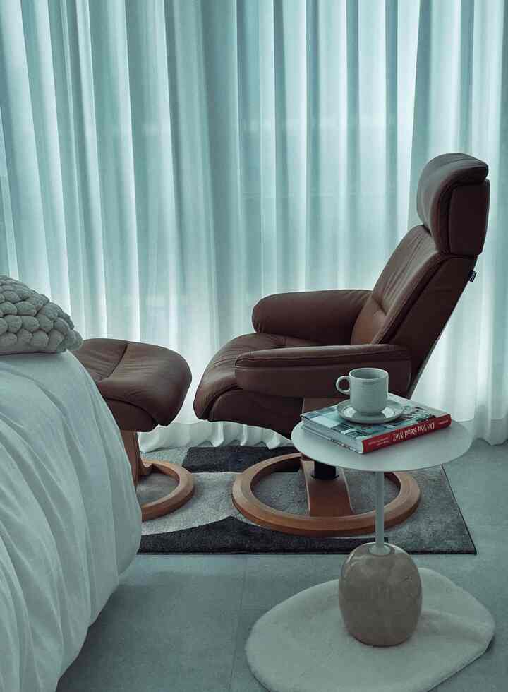Bedroom with white curtains as background, beige recliner and white coffee table arranged in a minimal and natural style space