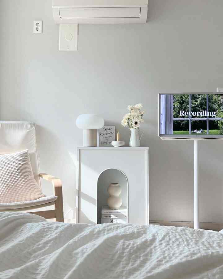White and ivory-toned bedroom featuring modern, simple wall fireplace console and objets, creating a cozy atmosphere