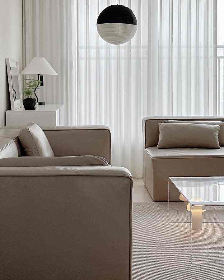 White and beige toned living room featuring simple modular sofas and a transparent acrylic table in a modern, clean setting