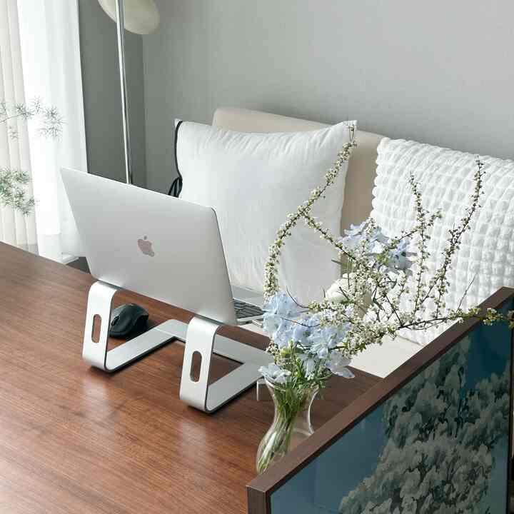 White and brown toned living room featuring a walnut table, sky blue flowers in a glass vase, and a laptop on a simple modern setup