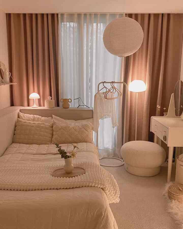 Beige and ivory toned cozy bedroom featuring curtains, stool, and warm lighting creating a harmonious space