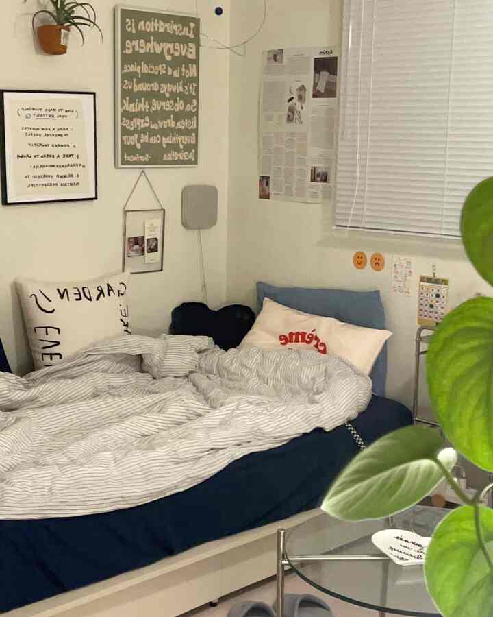 A cozy bedroom with white walls and a navy mattress, featuring green plants and framed wall art