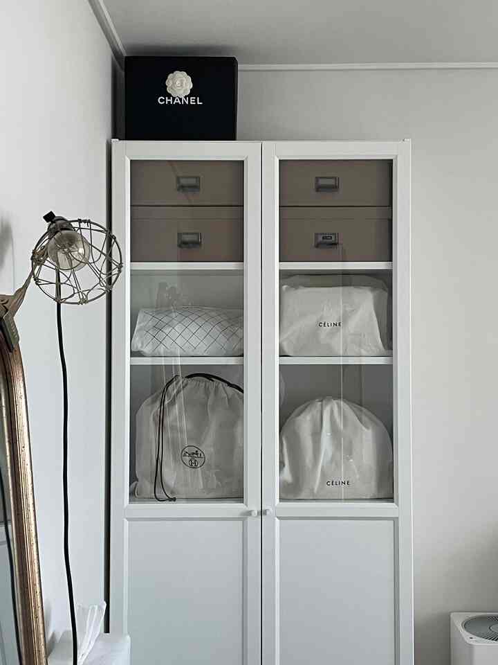 白を基調とした寝室の収納スペース、ガラス扉のきれいな白い収納キャビネットと整理された茶色の収納箱が配置された雰囲気あるインテリア