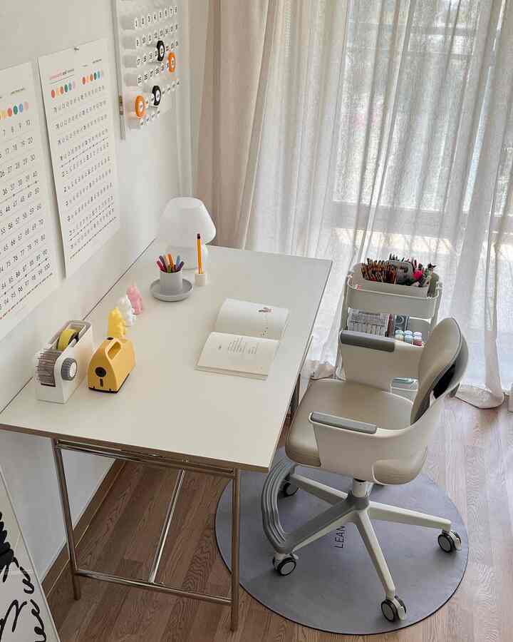 白い壁とベージュのカーテンがある子供部屋、子供用デスクとオフィスチェア、円形ラグが配置された雰囲気のあるインテリア