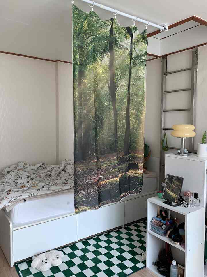 Cozy small studio bedroom with green forest print curtain centrally hung, featuring white bed and storage cabinet