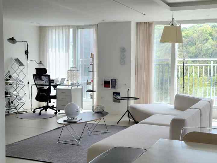 Modern living room in white and gray tones featuring a large sofa and home office desk with a clean layout