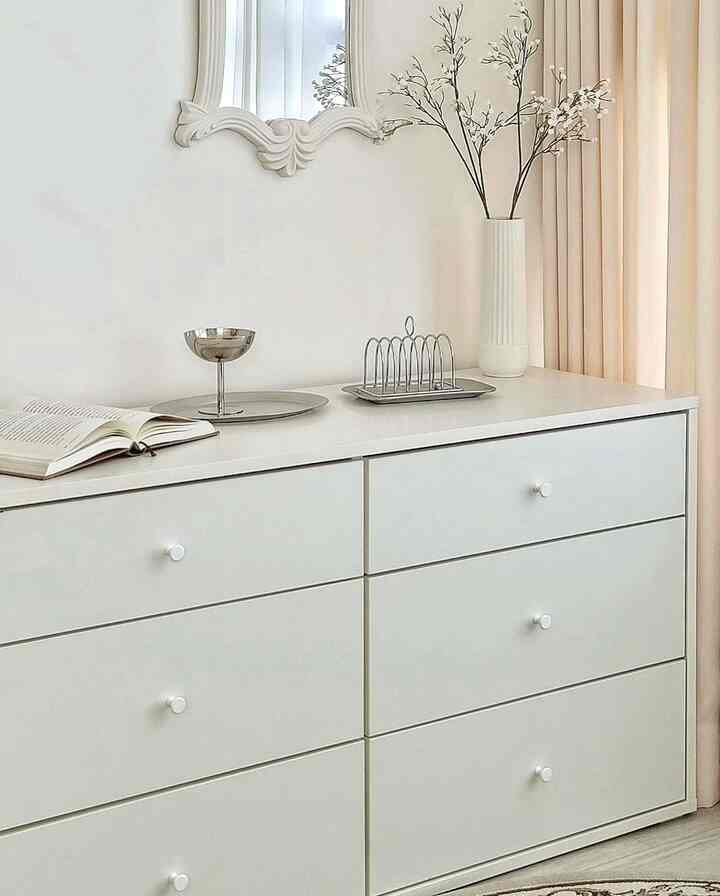 Minimal interior space with white and beige dresser featuring wall mirror and decorative vase