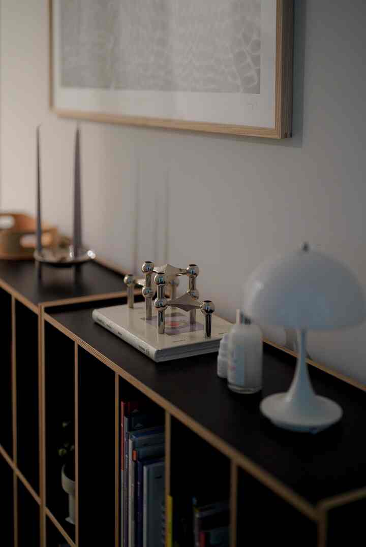 Modern minimal interior corridor featuring a black and wood tone bookshelf topped with a candleholder and lamp, with elegant decor