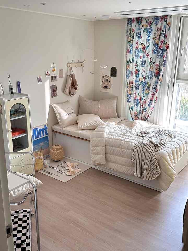 White and beige toned studio bedroom featuring a storage bed frame and floral curtains creating a cozy atmosphere