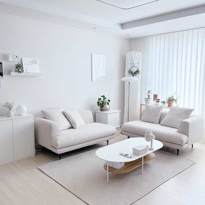 Bright white-toned living room featuring two cream modular sofas and a white coffee table creating a clean, cozy atmosphere